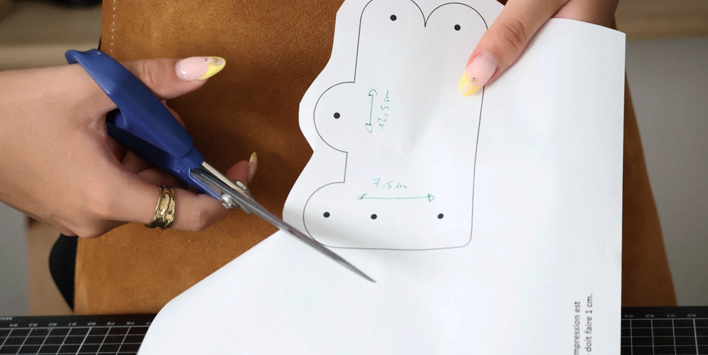 Cutting out the paper pattern for the original boobs key case on a piece of leather